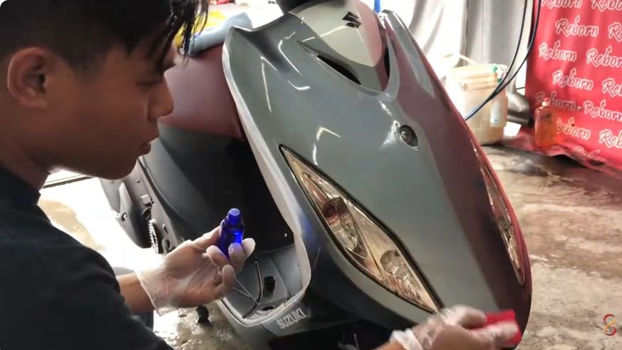 原片人員手持小瓶與工具，在機車前方車殼進行局部施作